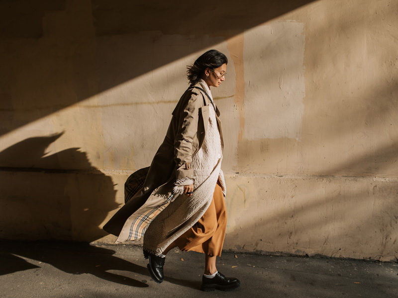 Mujer caminando bajo el sol de otoño con un abrigo.
